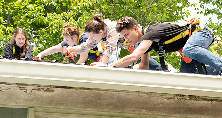 几个学生戴着安全带并在屋顶上工作。